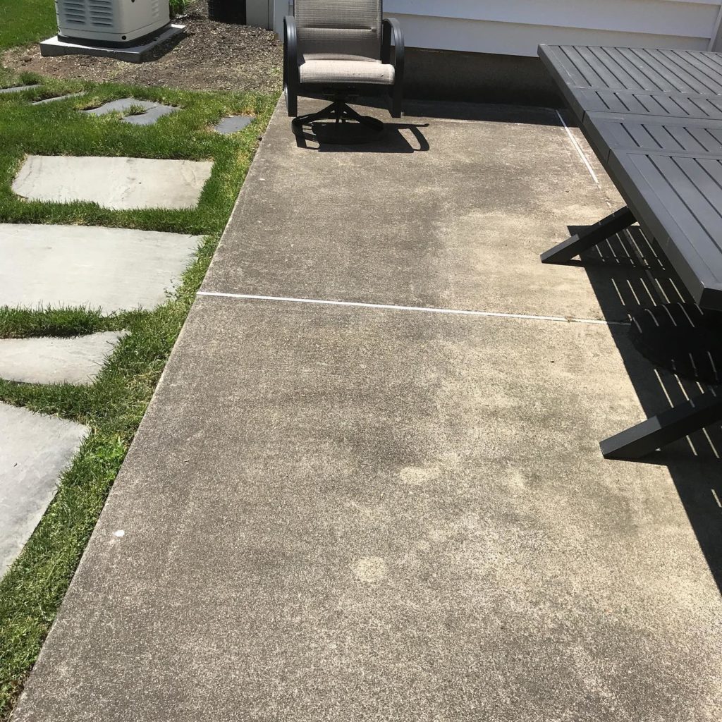 Concrete patio with outdoor furniture, adjacent to grass and stepping stones.